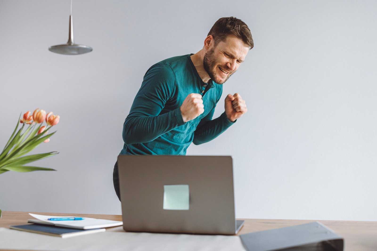 Excited man full of energy sitting behind laptop with big smile on his face. Overly happy person loo